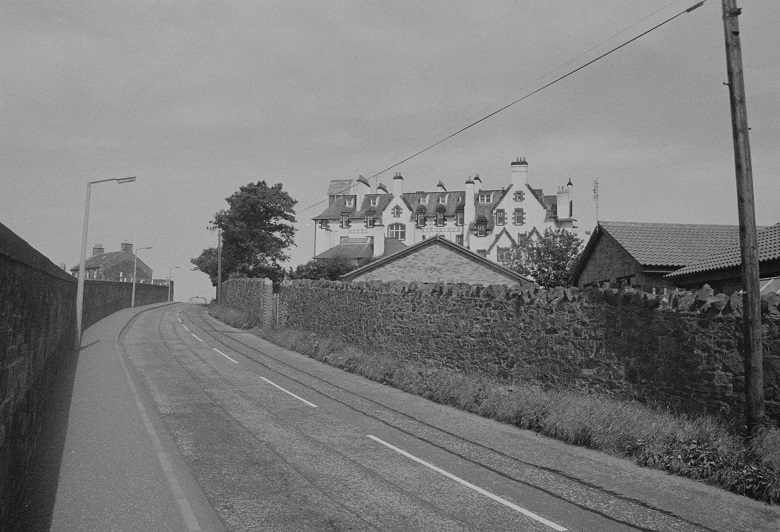 An empty road passing by the back of a large hotel building. The hotel is separated from the street by a high stone wall. 