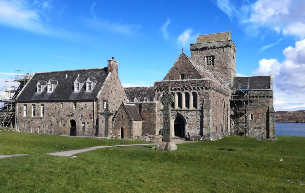 Exterior view of Iona Abbey on a sunny day. The abbey complex is complete with roofed buildings. It is small and not particularly ornate in comparison to other medieval abbeys.