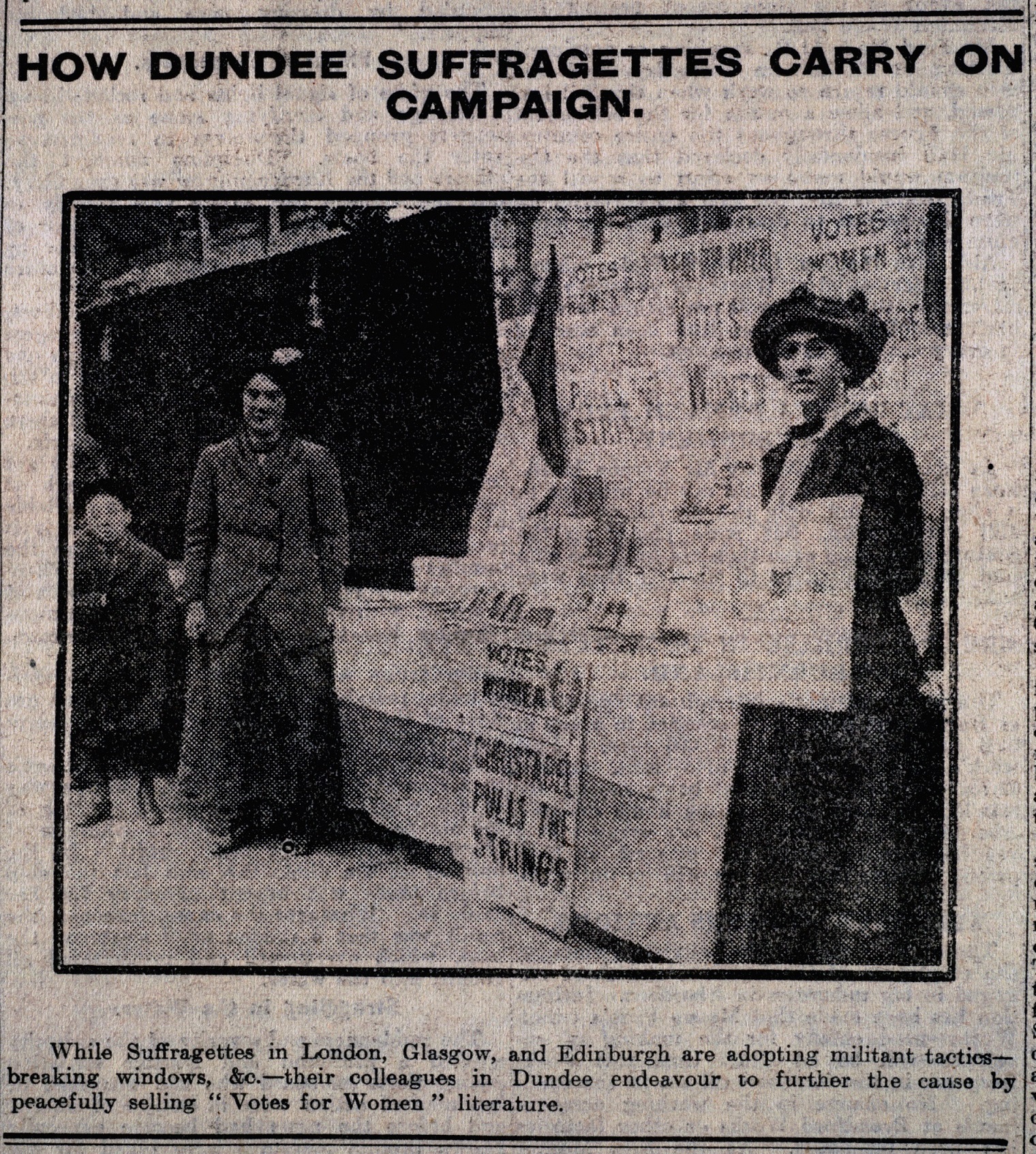 Black and white photo from a newspaper showing two women carrying suffragette signs. 