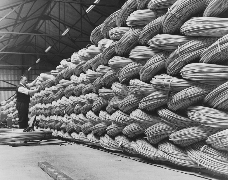 A worker inspects stacks of coiled metal wire in a large warehouse