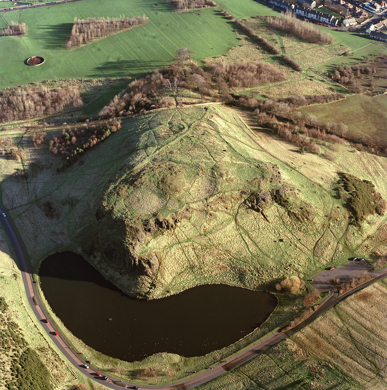 An aerial photo of a small rocky hill. Traces of human activity including pathways and fortifications are evident.