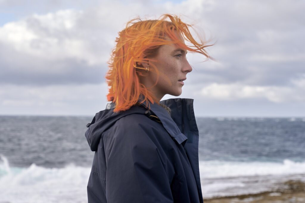 Film still of Saoirse Ronan as Rona from The Outrun looking over the water at Orkney.