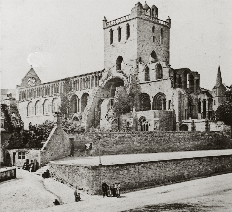 A historic photo of a group of people standing in front of the romantic ruins of Jedburgh abbey.