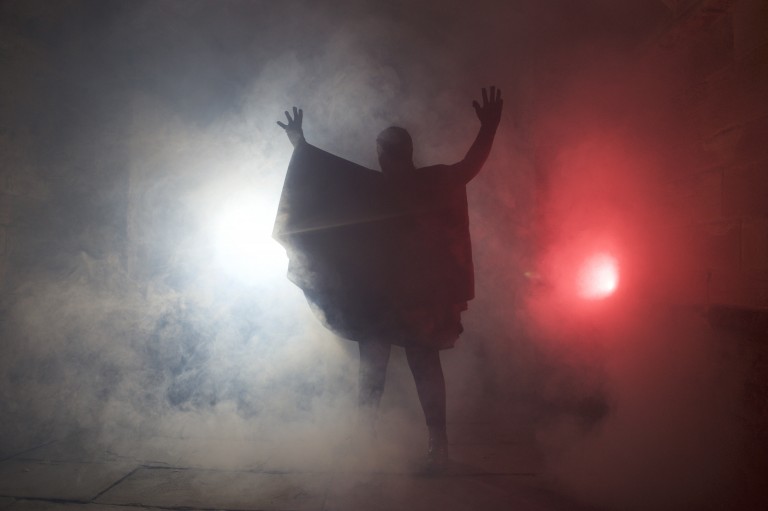 A cloaked figure, perhaps a vampire, emerges from fog at a Halloween event.