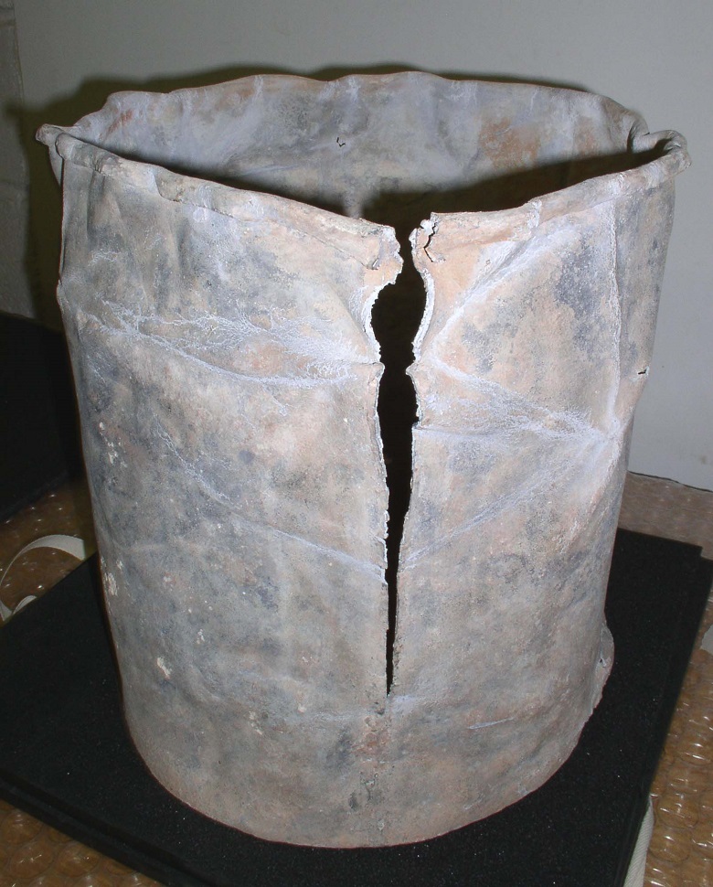 A battered lead casket with a split in the side. It looks a bit like a rubbish bin.