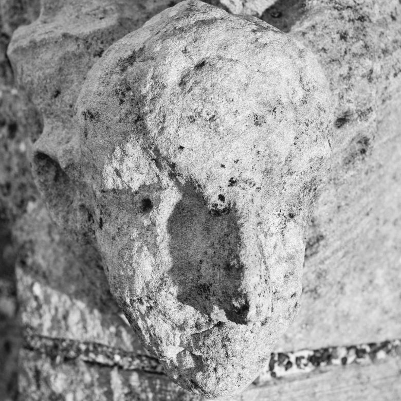 Close up of a carved stone "grotesque". It is the face of a bald man with a large nose, pointed ears, upwardly sloping eyebrows and pointed teeth. 