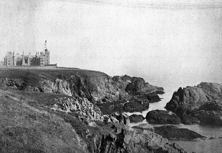 A black and white archive photo of a large, grand castle perched atop dramatic, rocky sea cliffs.