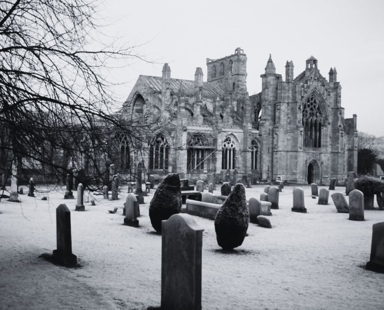 Black and white image of a ruined abbey with grave stones in the foreground