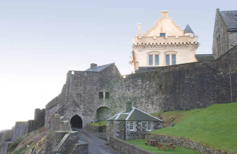 A medieval gate as part of a castle. A reconstructed palace roof is peeking up behind it.