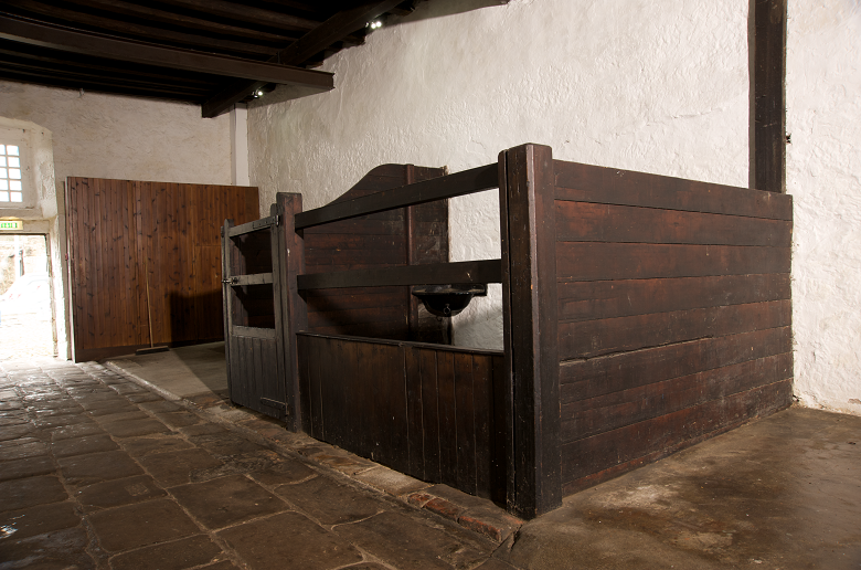 A stable block built by the 8th Earl of Morton in Aberdour Castle featuring whitewashed walls and pen made from large wooden beams. 