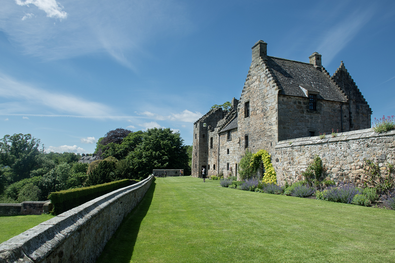 A castle building beside a terraced garden with smart lawns and flower beds 