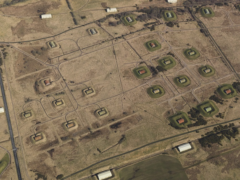 An aerial view of a factory complex showing small buildings surrounded by earthworks dotted around the site