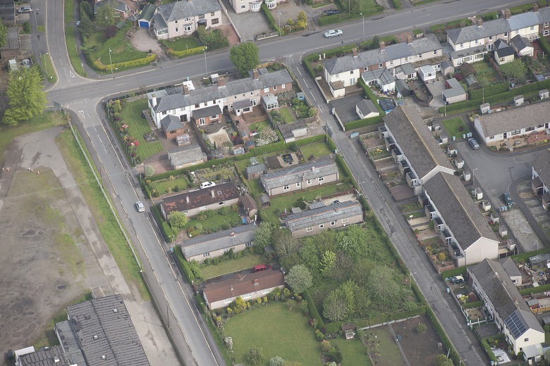 An aerial photo of streets and houses in the town of Gretna. Five of the houses are bungalows in the shape of long accommodation huts. 