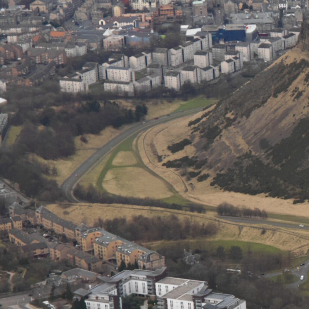 An aerial image of the park shows the Crags covered in gorse. The road runs around the foot of the Crags and on the other side of the road are a number of trees - almost a small woods.