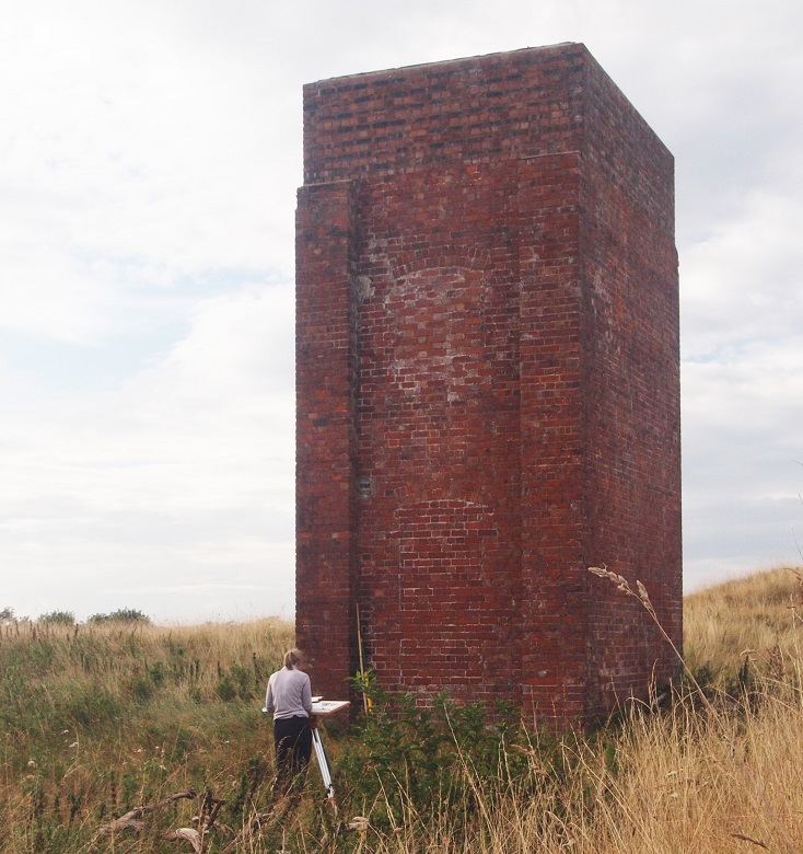 A surveyor working in front of a large red brick tower. 