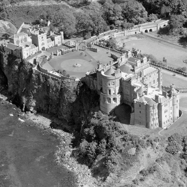 Aerial image of a lavish Georgian style castle on top of a cliff with formal gardens.