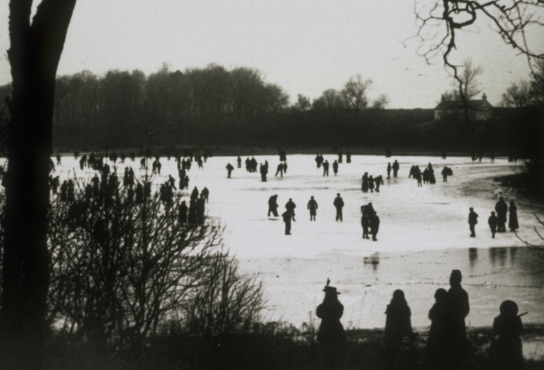 a black and white view of skaters on a pond. The contrast is very high but it's possible to tell they are in late 19th century fashions. The frozen surface is white with silhouettes of skaters on the ice and lining the banks.