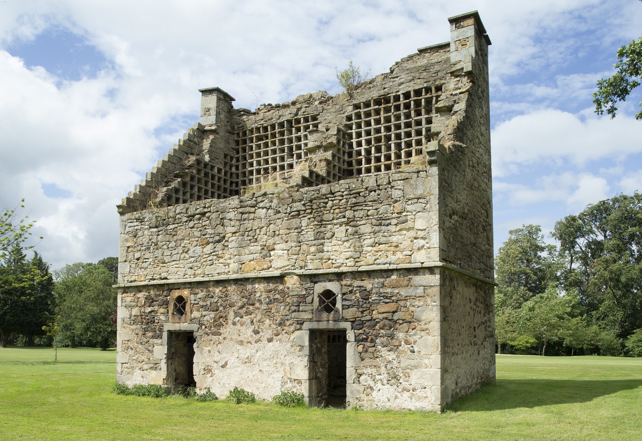 A ruined, roofless doocot. The walls are tilted to one side making it look like a lectern. It has the pigeonholes in them and two small doors.