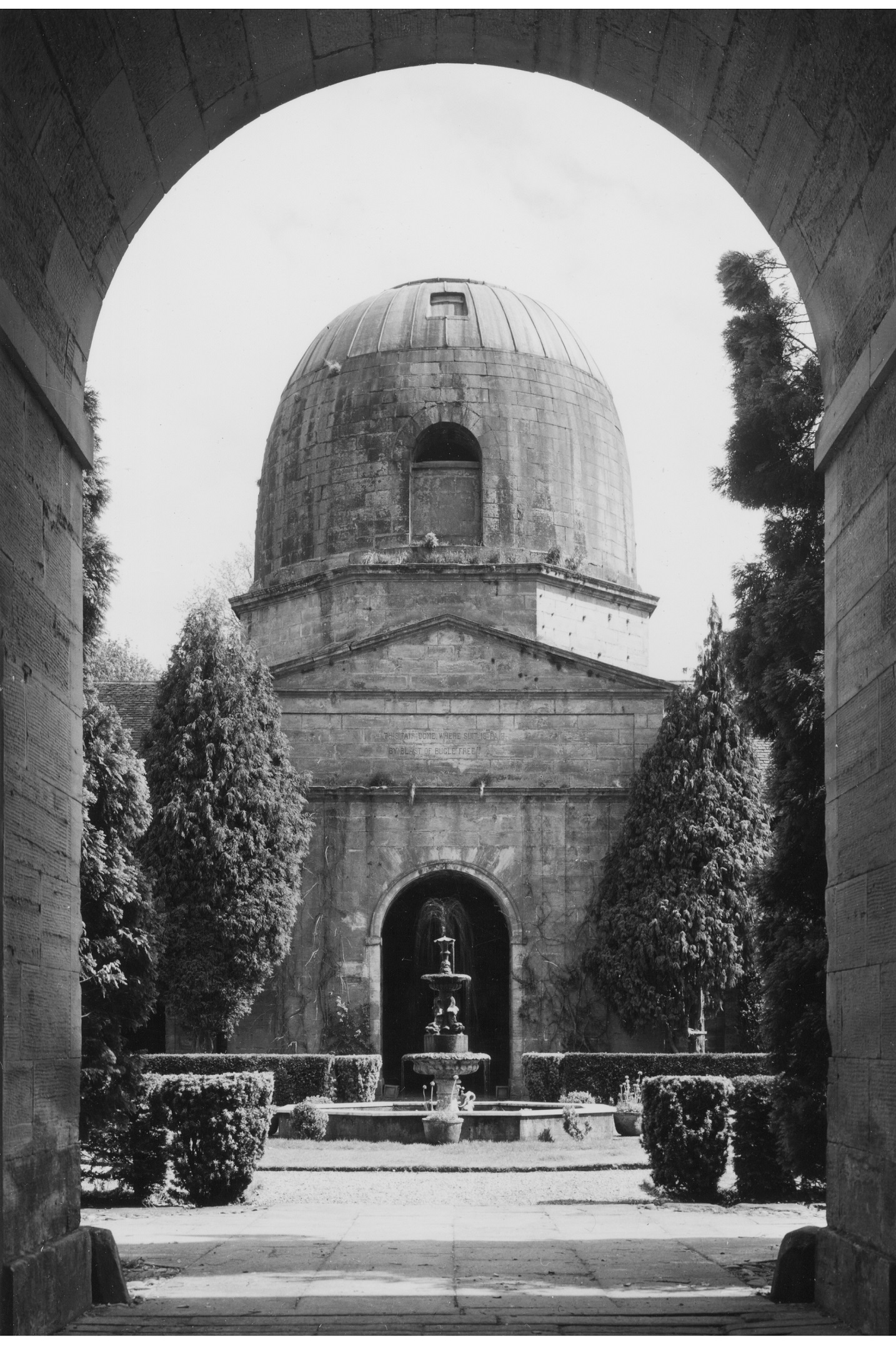 Black and white archive photo of a round, domed doocot. There is a fountain in front of it. 