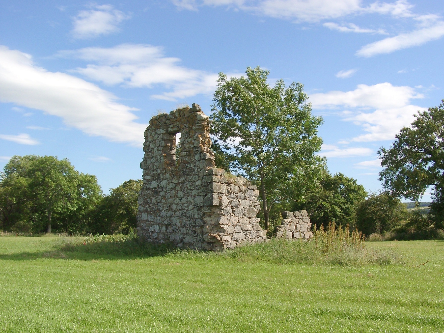 A small ruin of a doocot. Only the wall with the small window and the foundation are left.