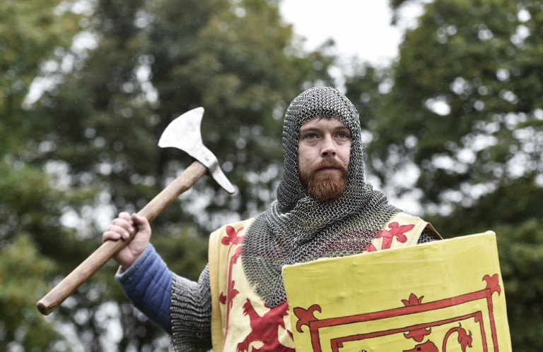 Bearded man in chain mail with lion rampant shield holds up an axe as if ready to strike