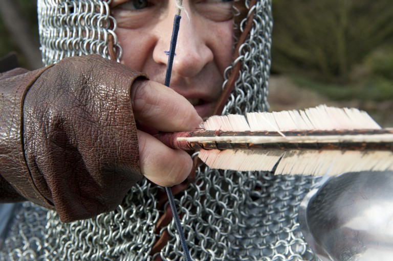 Close up of man in chain mail drawing back an arrow