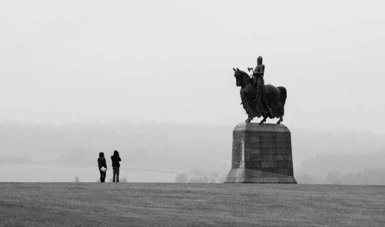 silhouettes of two people standing in front of a plinth, taller than them both, with a stature of a man on horseback atop it