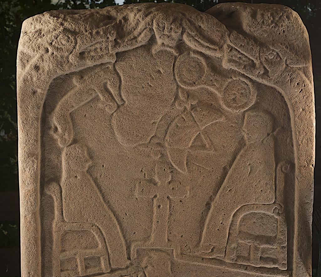 close up of a stone with two seated figures facing each other over a cross