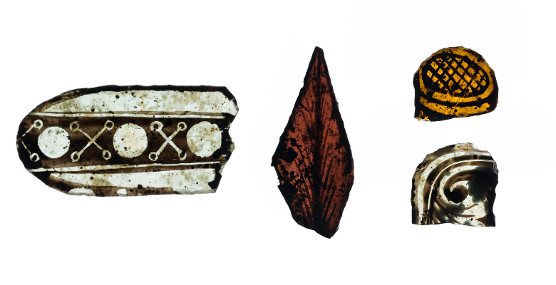 Four fragments of stained glass of varying shapes, colours and sizes. In one, a black and clear design, which looks like part of a border, has simple alternating crosses and circles. Another is diamond-shaped and amber in colour with a design that looks like a feather or leaf veins. A small yellow fragment has some black detail showing an oval with a lattice design. And the final fragment is clear with some curved and swirling lines on it.