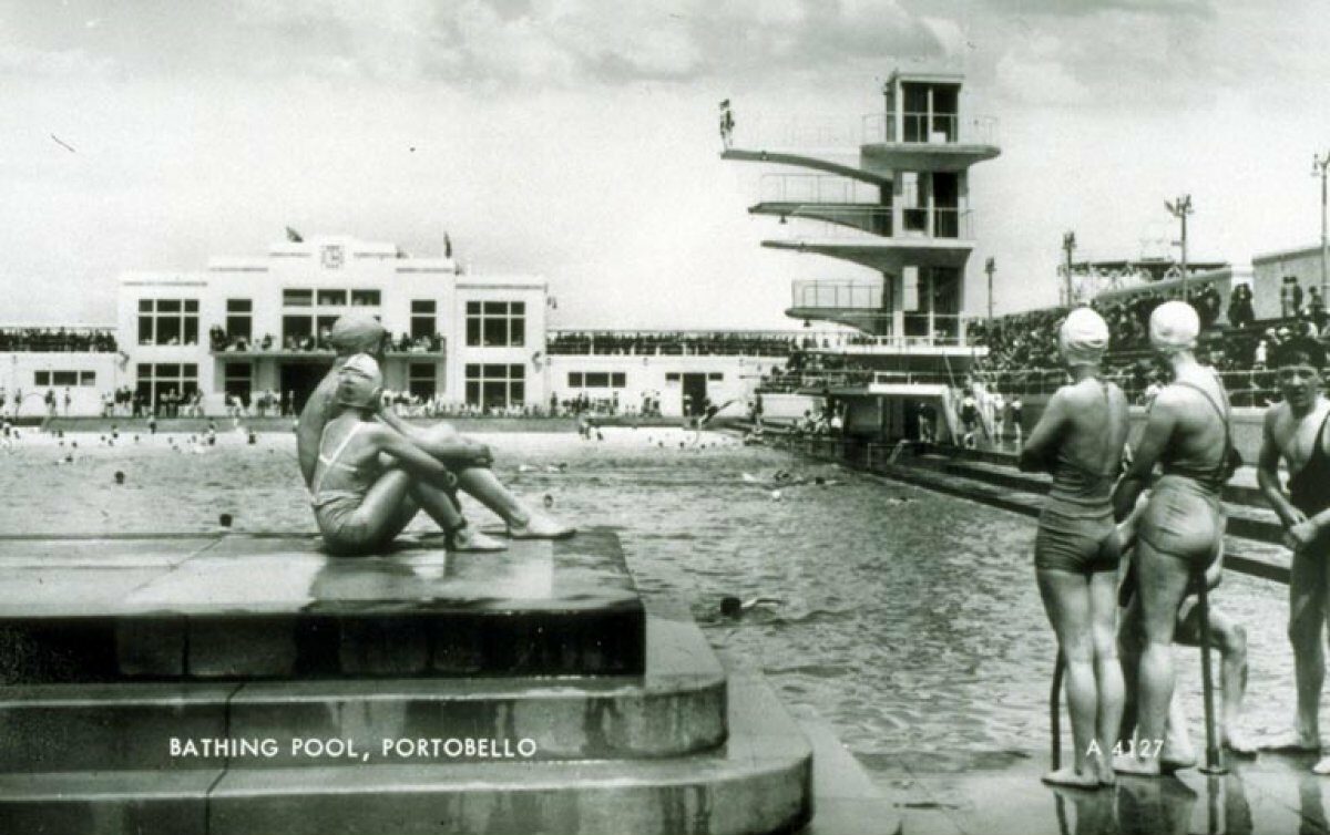 Black and white archive photo showing portobello swimming pool and the jumping board int he background. There are several swimmers too.