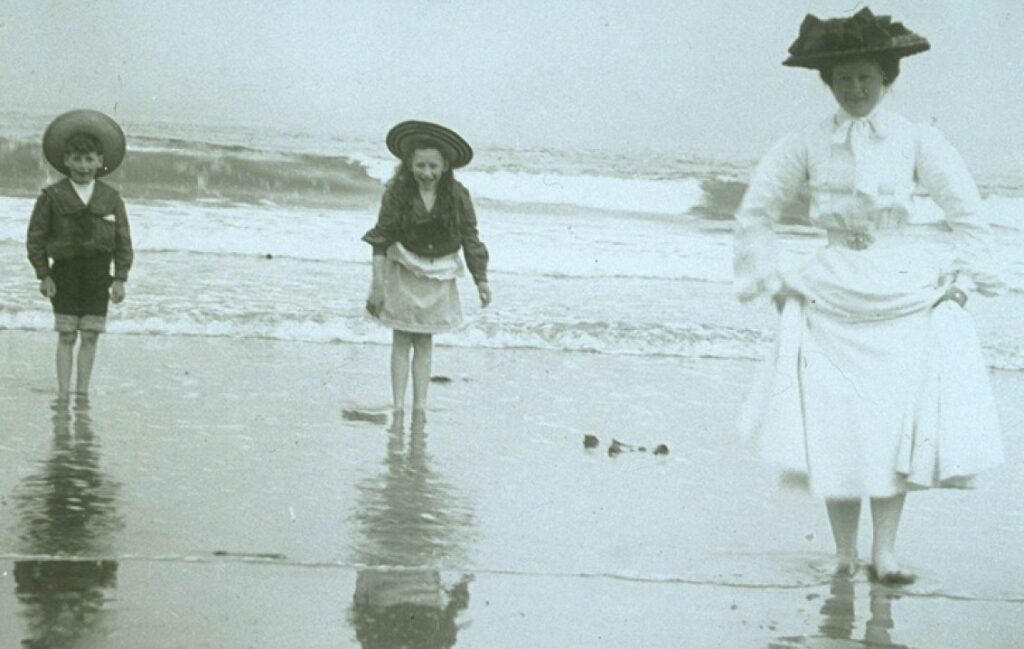 A black and white archive photo showing an Edwardian family by the beach with their feet in the water.