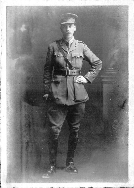 MacRae in military uniform, he is facing the camera and has his hand on his waist. The photo is black and white.