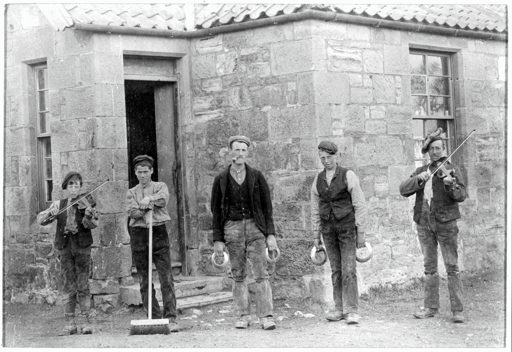 Posed photograph of five farm workers, the two men in the middle are holding quoits.