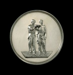 A silver medal, with two people in the centre. One is holding a quoit. 