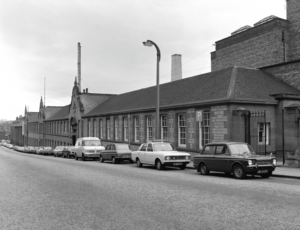 A factory next to a street, with cars parked alongside it.