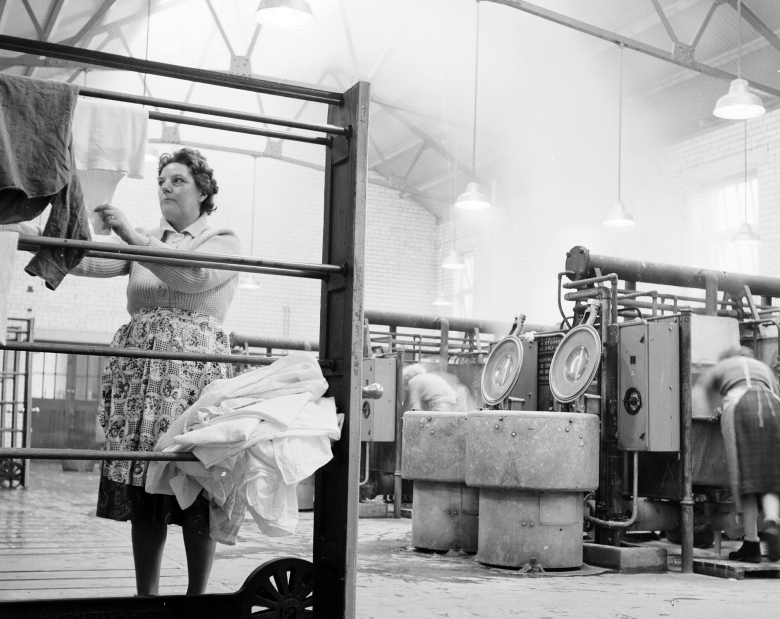 A woman hanging up laundry in a washhouse, it is foggy in the background.