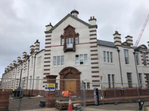 The front of a large white and brown building, there are fences in front of it.