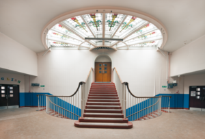 A hallway, with stairs leading to a door. There is a circular window.