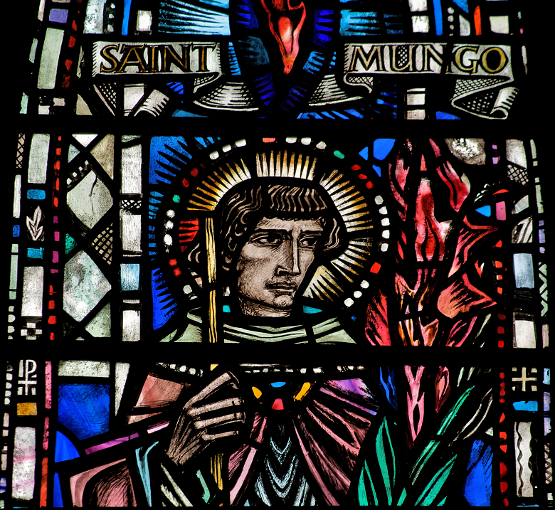 Stained glass window depicting Saint Mungo. He is in middle age and clean shaven with a halo of light around his head. He carries a staff. His name is written on a scroll above him.