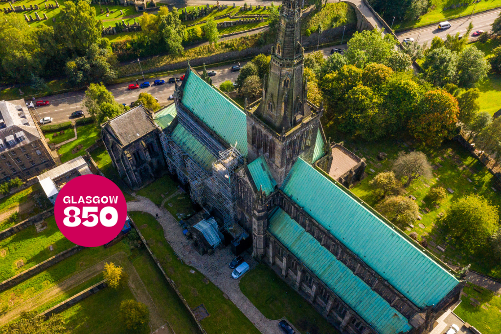 An aerial view of Glasgow Cathedral, a large Gothic-style church with a green copper roof. The cathedral is surrounded by trees and greenery, with a road and cars visible in the background. A pink circular graphic on the left side of the image contains the text 'GLASGOW 850'