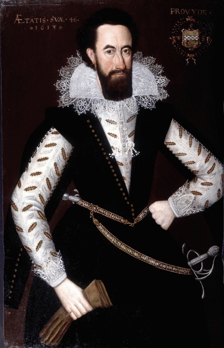 Portrait of a bearded man in elaborate 17th-century attire, wearing a black doublet with gold buttons and lace-trimmed collar and cuffs. He holds gloves in his left hand and rests his right hand on his hip. A sword hangs from his gold-embroidered belt. The background is dark, highlighting the subject’s features and clothing.