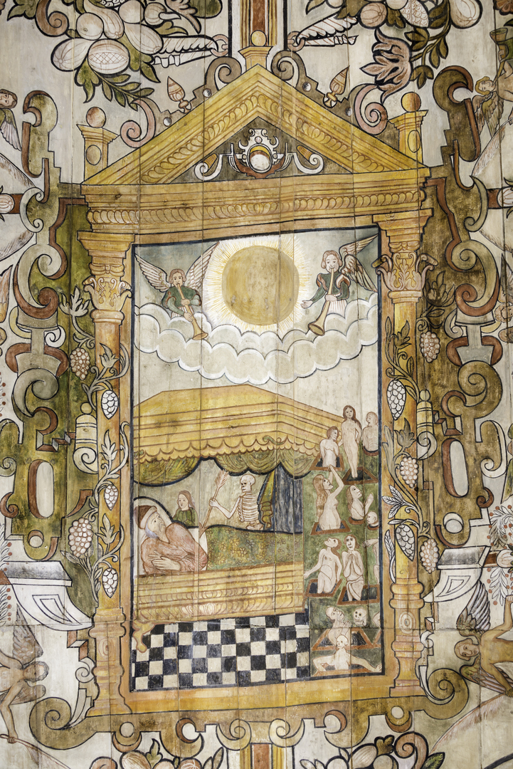 Ornate painting framed by a classical architectural structure with columns and a pediment. The central scene shows a figure lying in a covered four-poster bed. Beside the bed is a loved-one keeping a bedside vigil. Next to them is the figure of a skeleton with a large spear about to stab the figure in bed. Above the bed is a radiant sun flanked by two angels with trumpets. To the right, smaller figures are depicted in the Rapture, rising from their graves in various poses, including standing, kneeling, and sitting. The background is richly decorated with floral and vine motifs, including grapes and leaves.