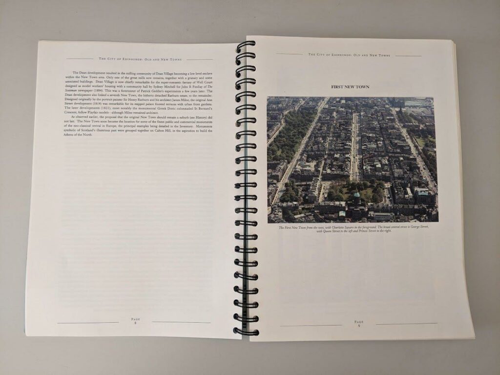 An open document on a table, the left page has black text, the right page an image of a city from above with streets in a rectilinear grid pattern.