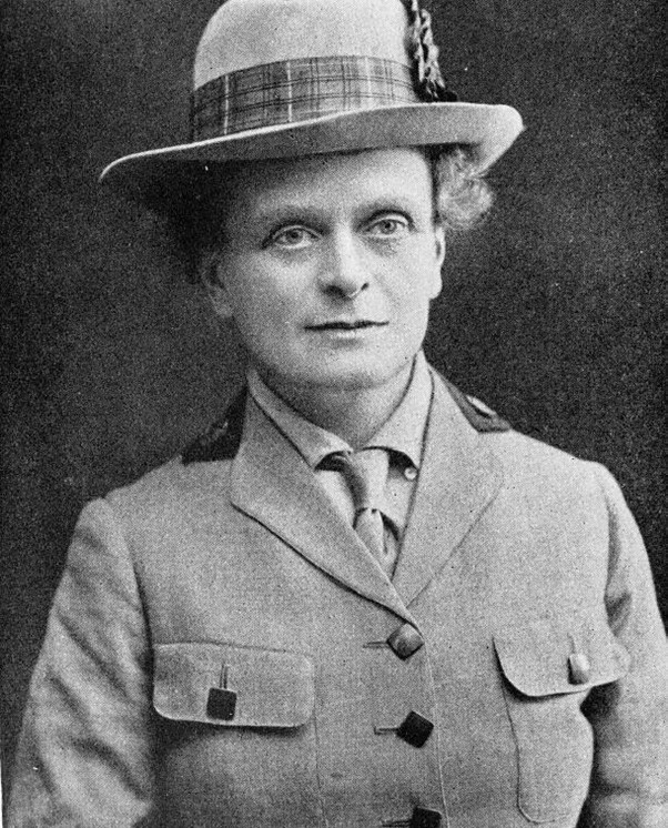 Elsie Inglis, a woman wears a formal outfit, with shirt, tie and jacket. She is wearing a hat and looking past the camera.