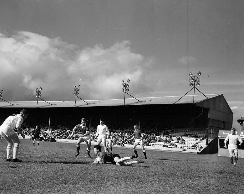 Men playing football at an outdoor stadium during daytime. One person is on the floor with the ball.