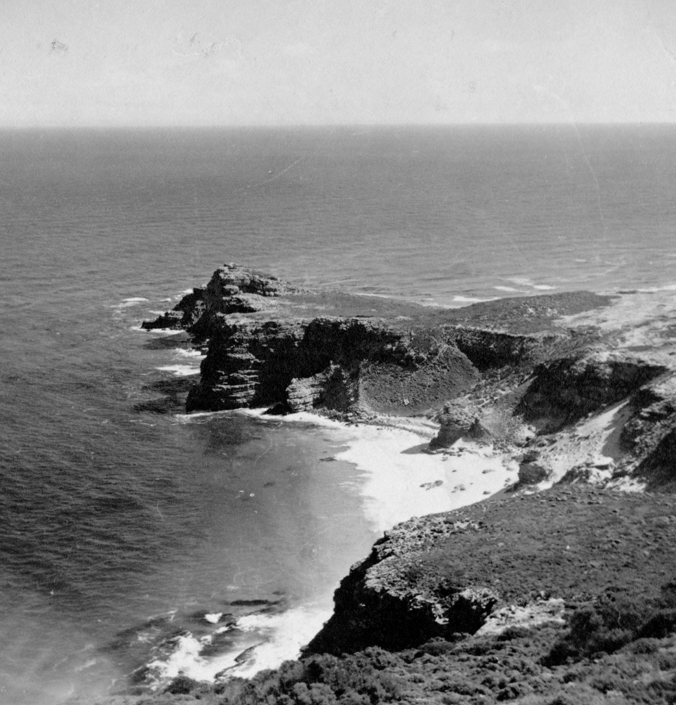 black and white photo of a sandy bay and a rocky outcrop surrounded by the ocean
