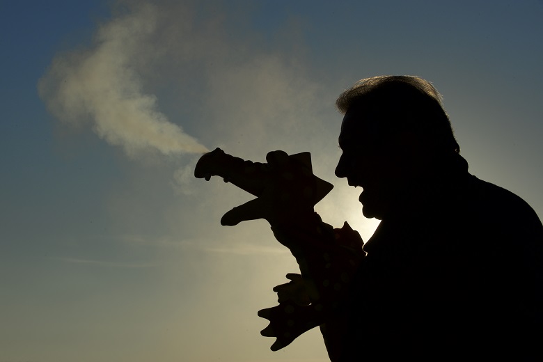 Silhouette of a person holding a puppet of a dragon, with visible breath forming a mist in the cold air against a clear sky background.