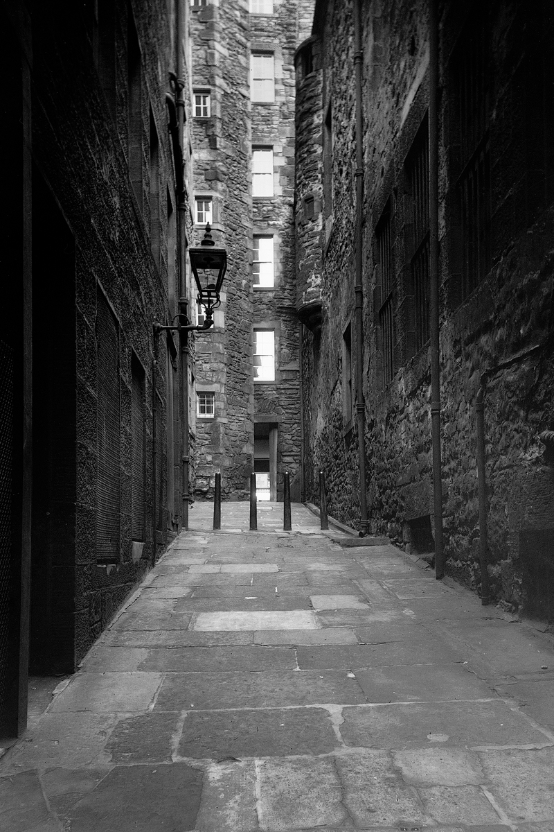 Black and white archive image of a close in Edinburgh. You can see a street light and looming walls