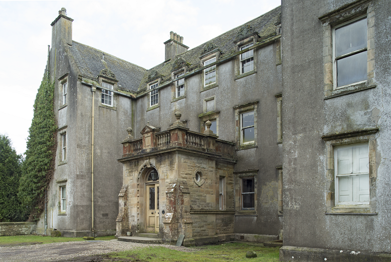 Front view of Bannockburn House, a large historic stone building with three stories and a pitched slate roof. The central section features an ornate entrance with a carved stone doorway. The exterior walls show signs of age and weathering, with some windows boarded up or missing glass.