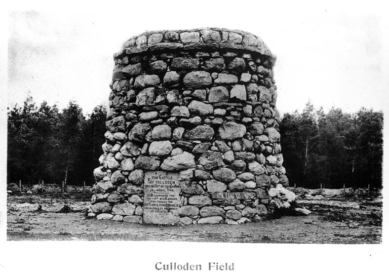 A black-and-white photograph of the large stone memorial cairn at Culloden Battlefield. The circular structure is built from irregular stones and has a flat top. A plaque on the front reads: “The Battle of Culloden was fought on this moor 16th April 1746. The graves of the gallant Highlanders who fought for Scotland & Prince Charlie are marked by the names of their clans.” The cairn stands on open ground with a line of trees in the background.